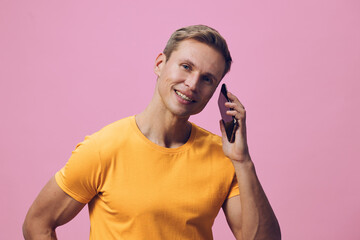 Smiling man wearing orange t-shirt talking on mobile phone isolated on pink background, casual...