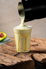 Creamy avocado smoothie poured into a clear cup with honey drizzle, set on rustic wooden table