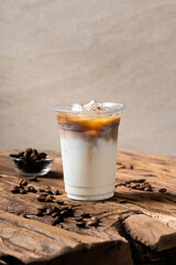 Iced latte with layered milk and espresso in a clear plastic cup, served on a rustic wooden table with scattered coffee beans