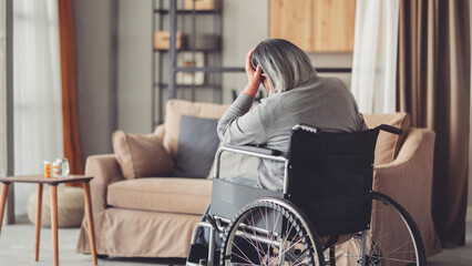 An elderly woman in a wheelchair covers her face with her hands	