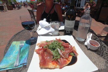 Outdoor patio dining with prosciutto pizza, wine, and water