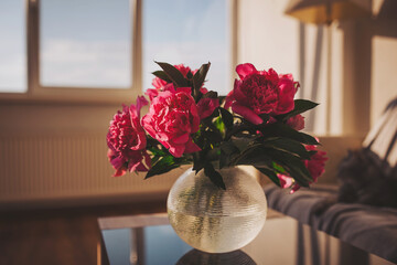 Vibrant peonies bask in golden sunlight on a stylish table, creating an atmosphere of warmth and serenity in a modern living space
