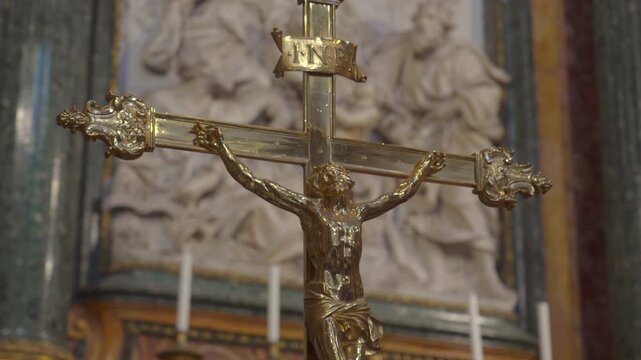 Close up of golden crucifix with figure of Jesus Christ and INRI inscription against blurred marble relief background inside ornate historic European church
