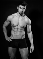 Naklejka premium Handsome bodybuilding man posing shirtless on black background flexing muscles and six pack after a workout