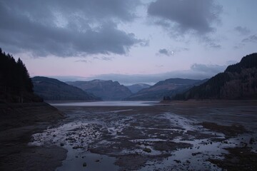 Obraz premium A tranquil, twilight view of a receding reservoir. Mountains frame a dried-up lakebed