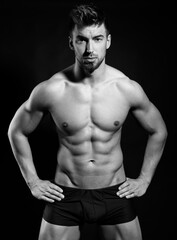 Obraz premium Handsome bodybuilding man posing shirtless on black background flexing muscles and six pack after a workout