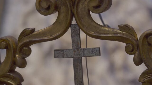 Close up of weathered metal cross surrounded by detailed golden scrollwork in historic European church interior