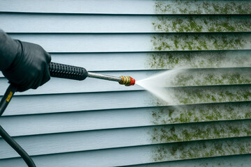 Pressure washer cleaning green mold from vinyl siding—clear before/after contrast. High-pressure water jet, home exterior maintenance, mildew and algae removal, power washing service.