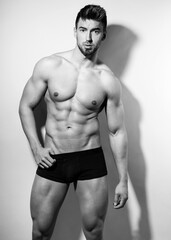 Handsome young muscular bodybuilding man posing in underwear with visible six pack in black and...