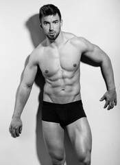 Handsome young bodybuilder posing shirtless in underwear and flexing his muscles 