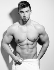 Handsome young bodybuilder posing shirtless after shower with towel in black and white