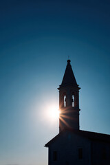 Fototapeta premium slender silhouette of church bell tower stands against backdrop of clear sky glowing under ultrabright sunlight