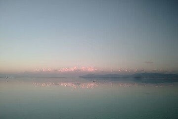 Calm lake reflecting a pale pink sunrise sky over distant mountains