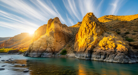Golden rocky hills bathed in the afternoon sun, a clear turquoise river below, thin white clouds like brush strokes.