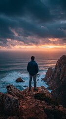 Fototapeta premium Man Standing on Cliff Overlooking Ocean Sunset