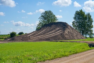 Large mound of soil on a green field with trees in the background under a bright blue sky with...