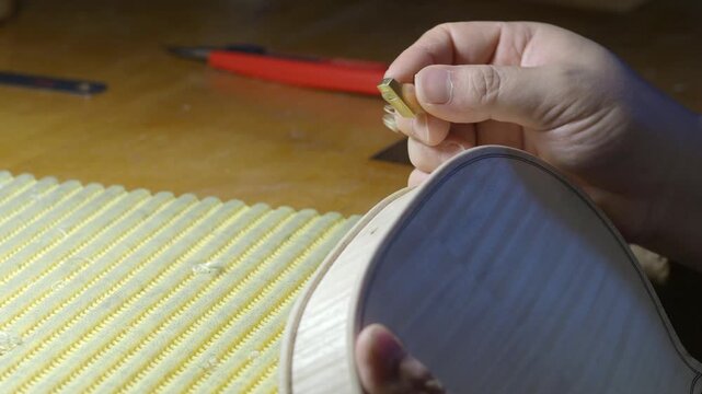 Skilled craftsman installing ebony tuning pegs on unfinished violin, showcasing meticulous woodworking technique and traditional lutherie expertise