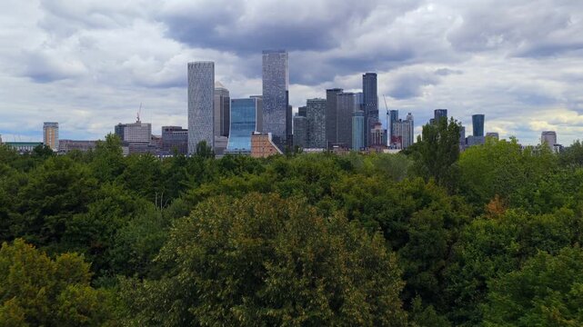 Aerial video of Canary Wharf skyline seen from the west, rising behind trees and low-rise homes.
