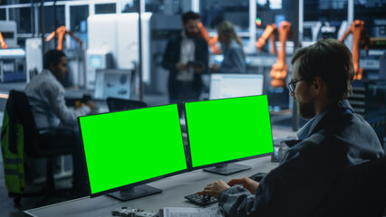 Caucasian Male Engineer Controlling Autonomous Conveyor With Robot Arms At Turbine Jet Engine Factory. Man Using Desktop Computer With Green Screen Chromakey On Display To Adjust Automated Production.