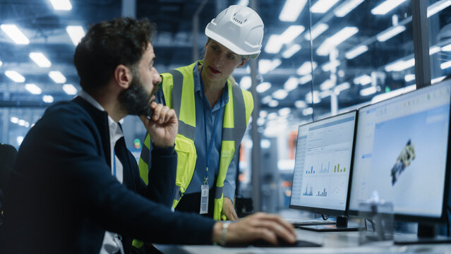 Car Factory Office: Latin Male Auto Engineer Showing Transmission 3D Render To Caucasian Female Automotive Production Supervisor On Computer. Automated Robot Arm Assembly Line Manufacturing Vehicles.