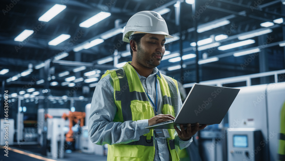 Poster portrait of an indian male engineer standing in factory office, using tablet computer at a machinery