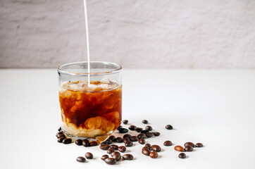 Latte coffee, Milk pouring from a milk jug into a glass of iced coffee with coffee beans on a white...