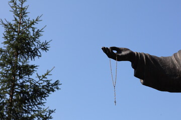 Statue with outstretched hand holding rosary against clear blue sky in tranquil outdoor setting