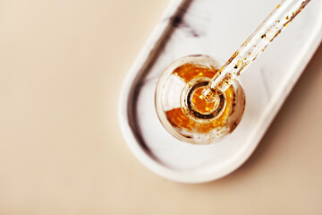 Top view of pipette dropping liquid with gold particles into glass bottle on marble tray