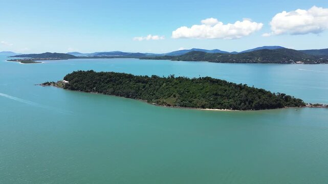Panoramic drone aerial scene of isolated tropical Ratones Island filled with Atlantic Forest trees and rocks with turquoise and cyan sea near Daniela Beach in Florian&oacute;polis, Brazil many birds in sky