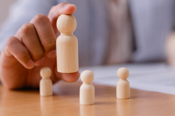 Leadership and teamwork concept with a business person arranging wooden human figures on a table,...
