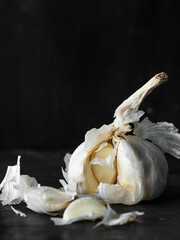 Whole garlic bulb with loose cloves and papery skin on a dark rustic surface