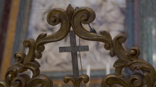 Small weathered metal cross framed by ornate golden scrollwork inside historic European church interior