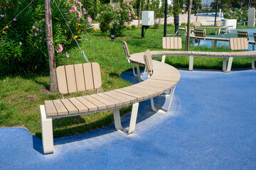 Improvement and landscaping of urban area. Curved wooden benches on blue rubber playground surface....