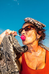 Stylish senior woman with leopard hat licking lollipop outdoors. Concept of bold self-expression,...