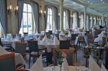 Formal and elegant ocean view dining room restaurant onboard luxury cruiseship or cruise ship liner with set tables in Art Deco interior design style and ceiling ambient lighting