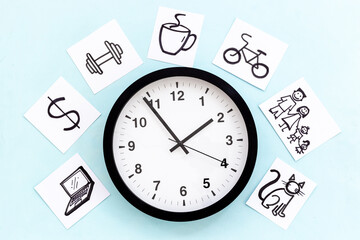 Wall clock and many paper cards with hand drawing of different life activities, top view. Time...