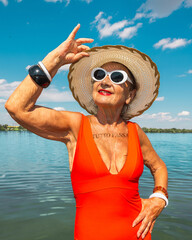 Elegant elderly woman in red swimsuit with drawn Italian phrase Everything Passes on chest, under sunny sky. Concept of active aging, summer lifestyle, travel leisure, personal style and empowerment.