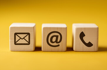 Three wooden cubes with icons of an email, phone, and letter on them, arranged in the order from left to right.