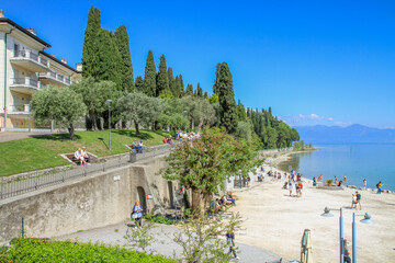Tourists enjoy a sunny day on the waterfront of Lake Garda, Italy, with picturesque views of the...