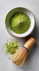 Matcha green tea powder in a bowl with a bamboo whisk, arranged on a gray background, showcasing the vibrant color and texture