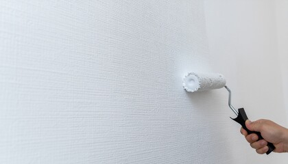 Close-up of a person's hand using a paint roller to apply fresh white paint to a textured wall, concept of home renovation and DIY.