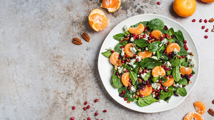 An appetizing festive salad of fresh spinach, tangerine, pomegranate and pine nuts on a plate. Copy...