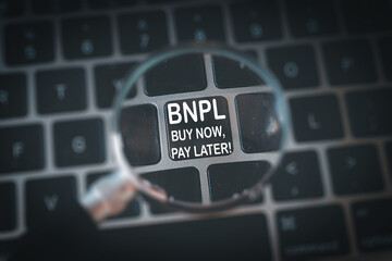 Top view of a magnifying glass highlighting the BNPL (Buy Now, Pay Later) option on a keyboard. A concept focusing on a key e-commerce feature and modern digital payment choices.