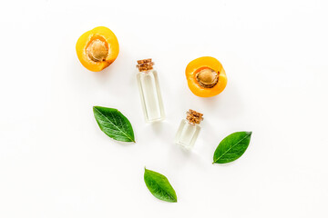 Apricot kernel oil among apricots and leaves on white background top view pattern
