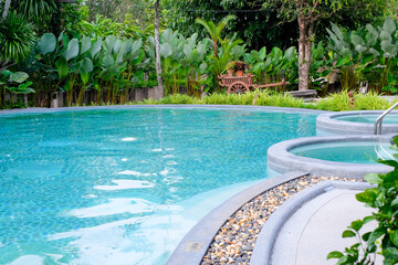 Outdoor swimming pool with round jacuzzi tubs surrounded by lush tropical garden, offering a relaxing and refreshing vacation atmosphere