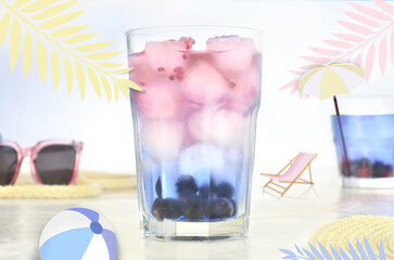 Big cocktail on the beach. Abstraction: big glasses and little beach ball, deckchair and parasol;...