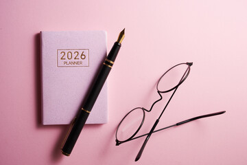 2026 planner,pen and eyeglasses against pink background.