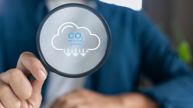 Hand holding a magnifying glass focusing on the CO2 neutral icon, concept of carbon neutrality, climate change mitigation, and environmental sustainability