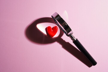 Red heart shaped with magnifying glass against pink background