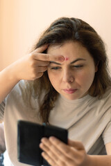 A teenage girl closely inspecting a blemish on her face in a bathroom mirror. Emphasizes acne care,...